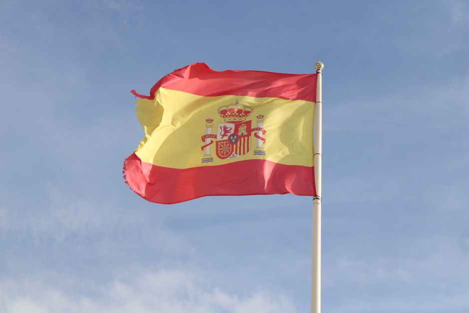 Bandera nacional española ondeando en un asta alta bajo un cielo azul claro en Andalucía.