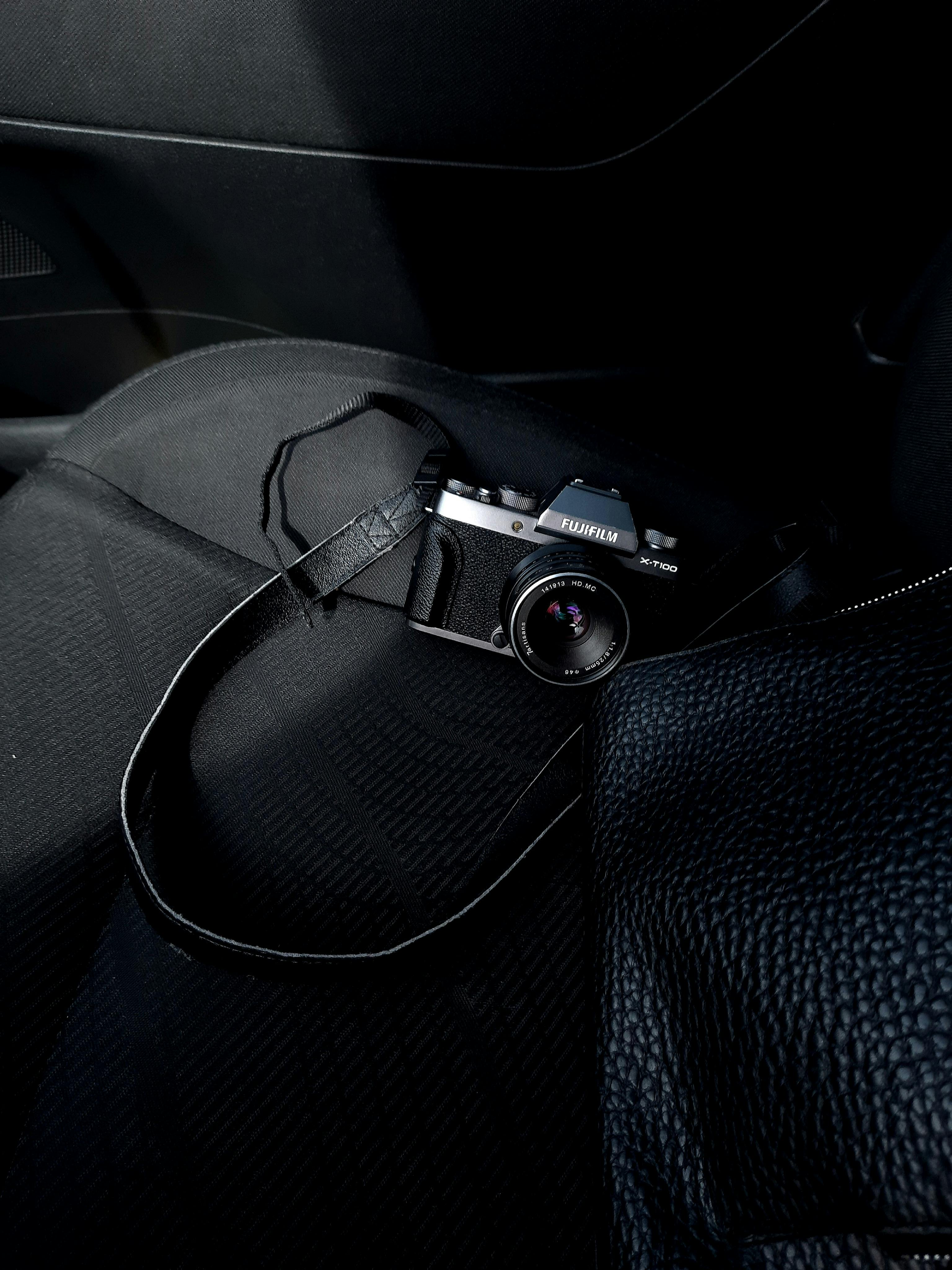 Close-up of a vintage film camera placed on a car seat alongside a textured black bag.