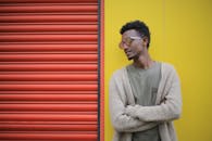 一位时尚男士戴着墨镜，靠在五颜六色的墙上，尽显潮流风范