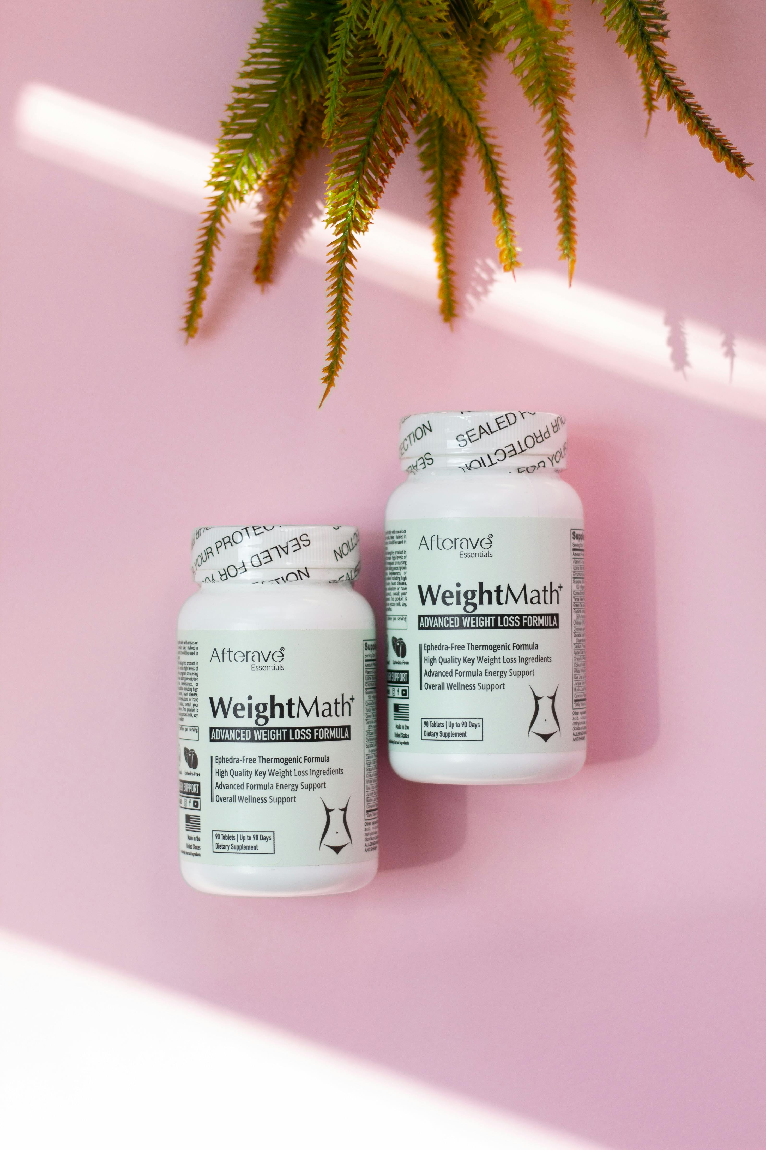 Capsules for weight management placed on a pink surface beside a fern leaf.