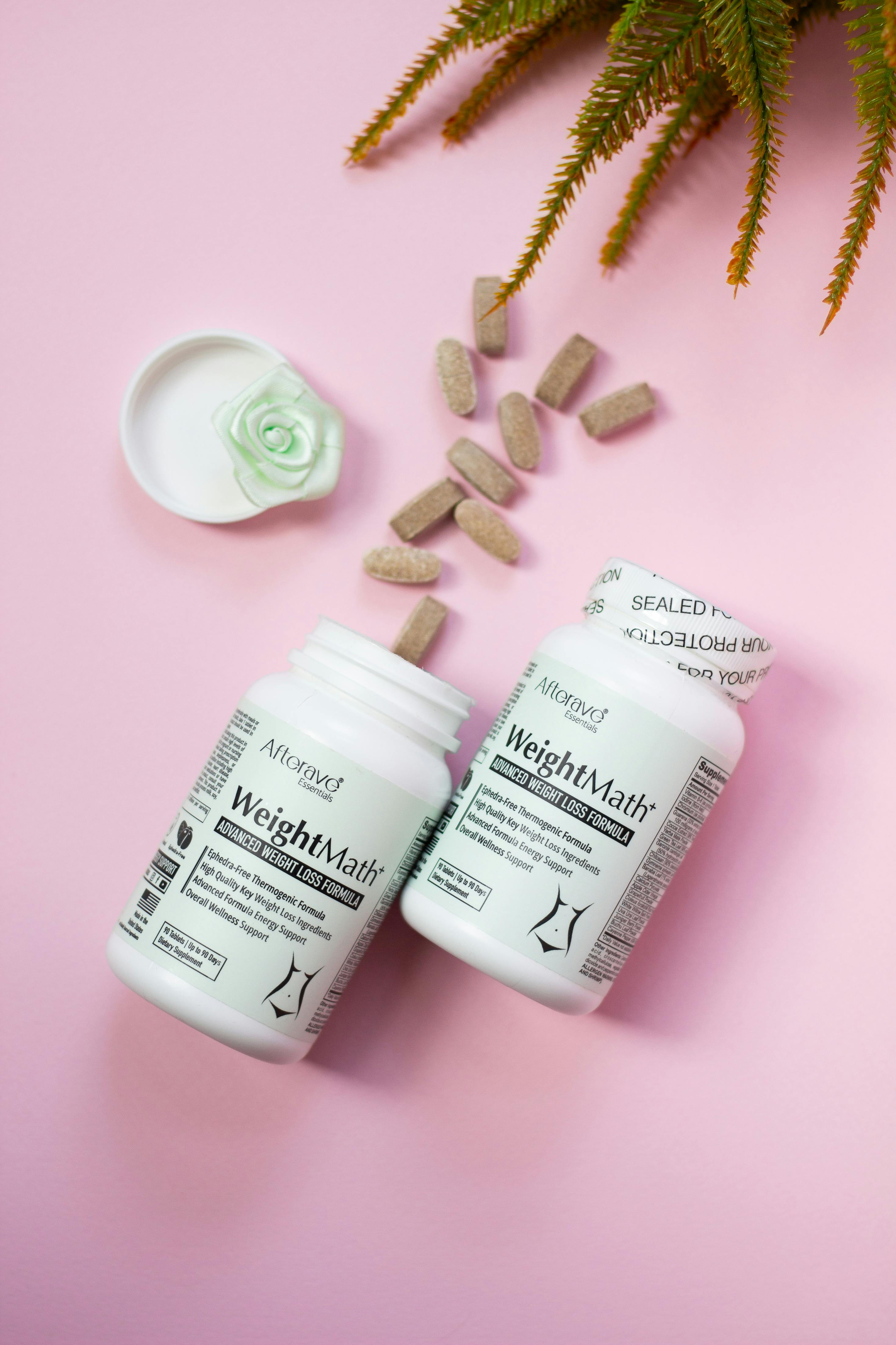 Weight loss supplement bottles and capsules on a pink background