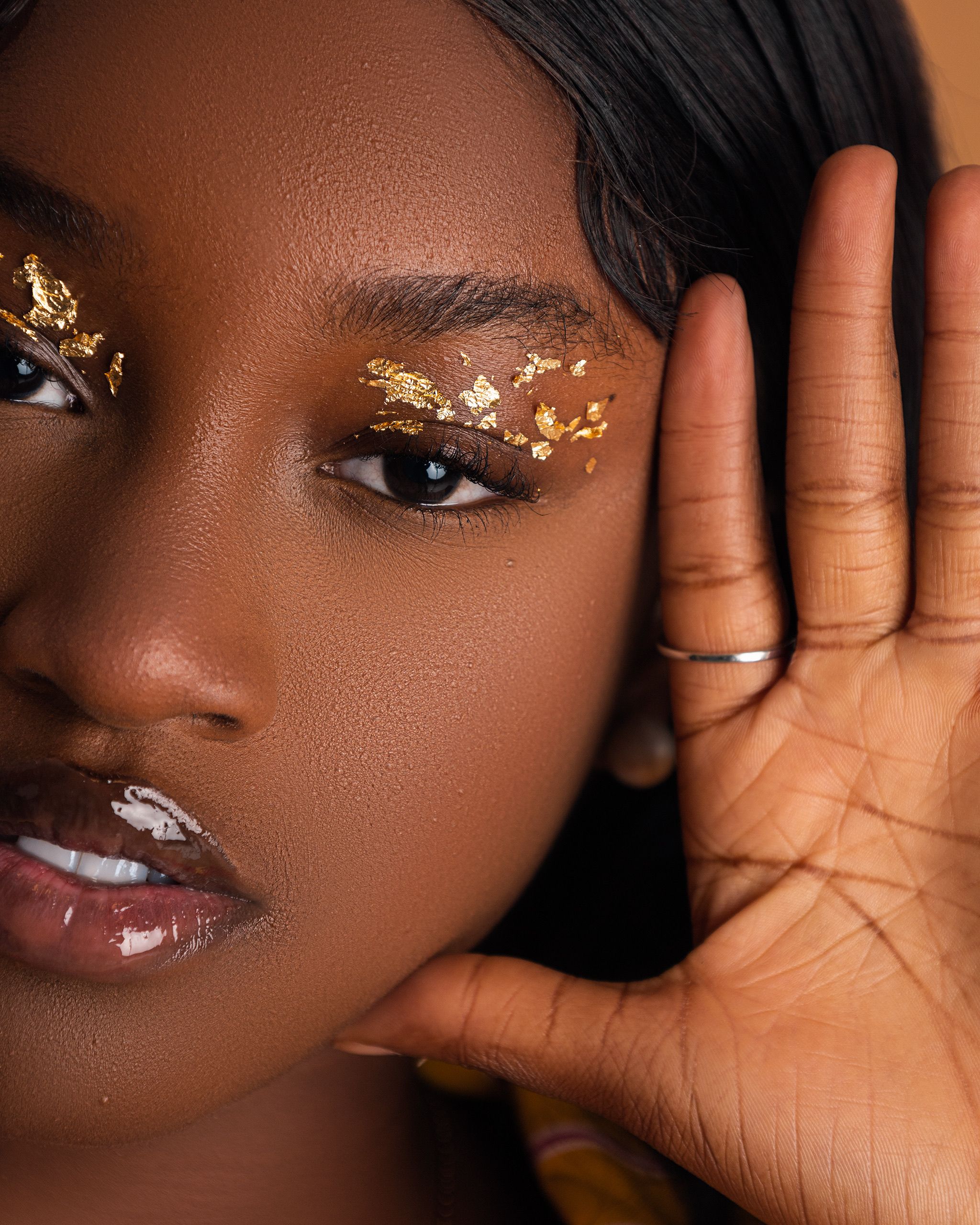 Close-up portrait of a woman with gold leaf eye makeup, showcasing beauty and creativity.