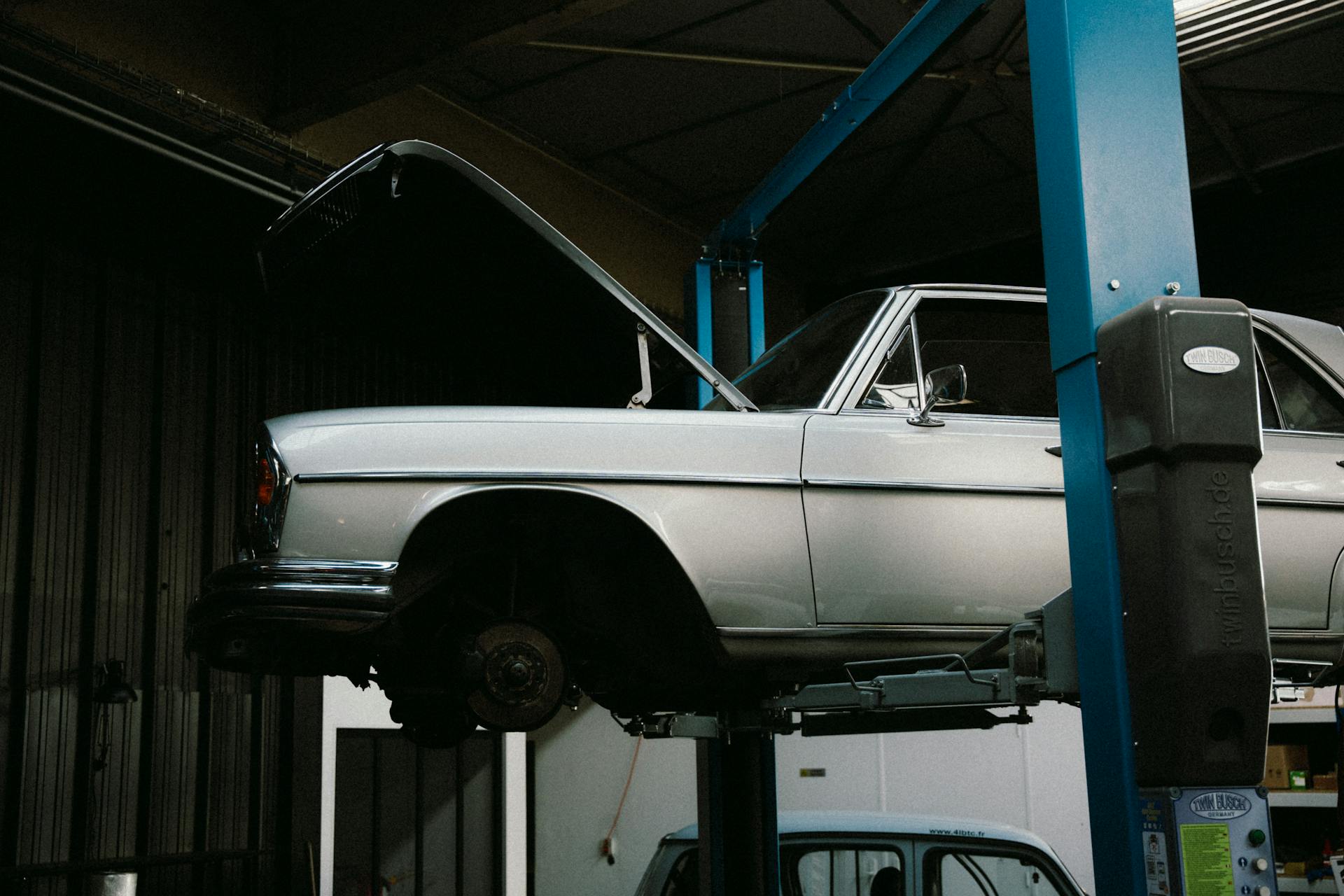 A vintage car being repaired on a hydraulic lift inside an auto repair shop.