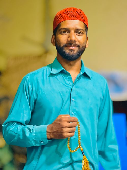 Free Portrait of a man in traditional dress holding prayer beads, smiling warmly indoors. Stock Photo