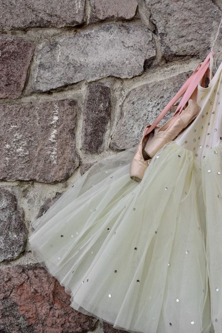 A delicate ballet tutu and pair of pointe shoes hang gracefully on a stone wall.