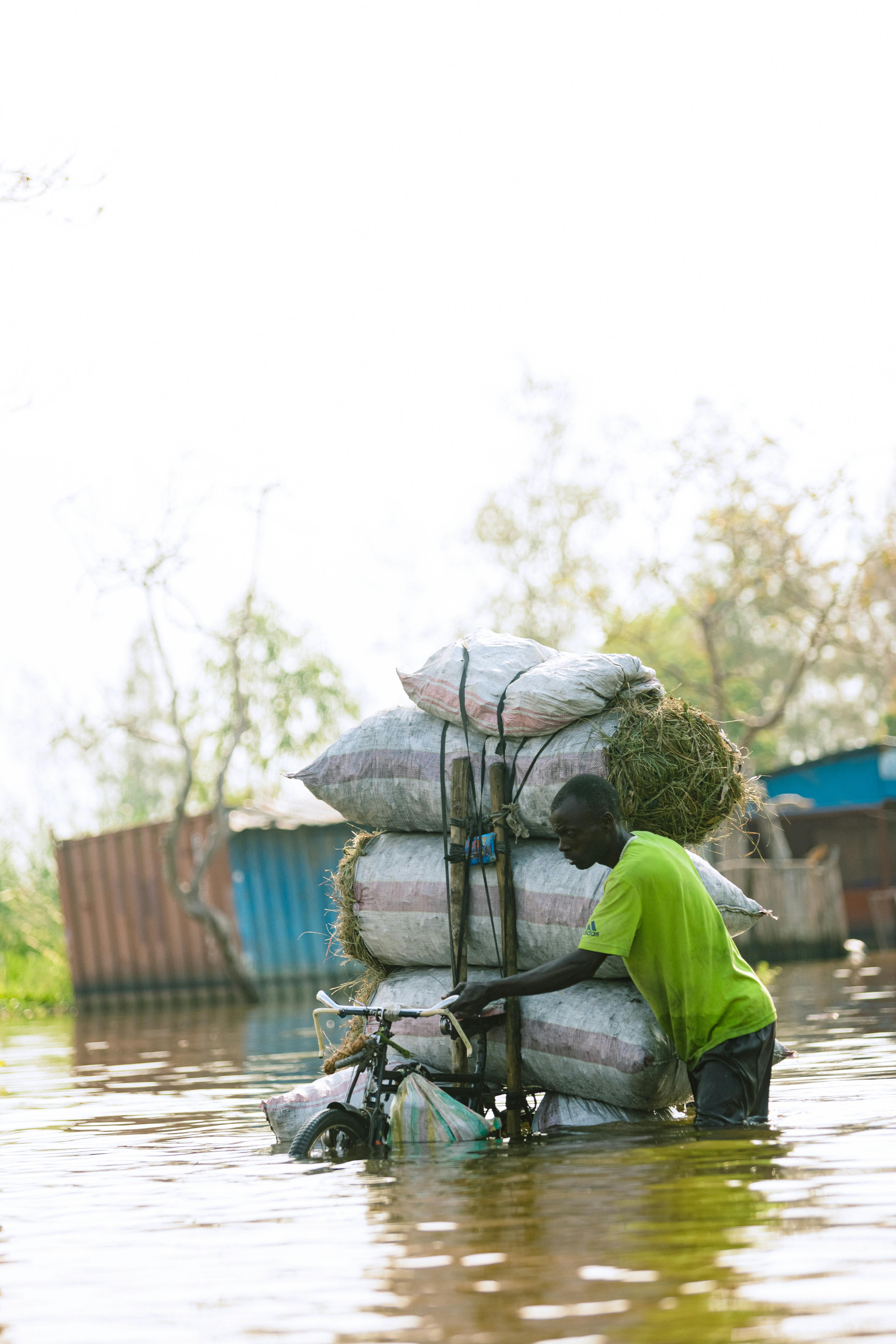 A man maneuvers a loaded bicycle through floodwaters, highlighting resilience.