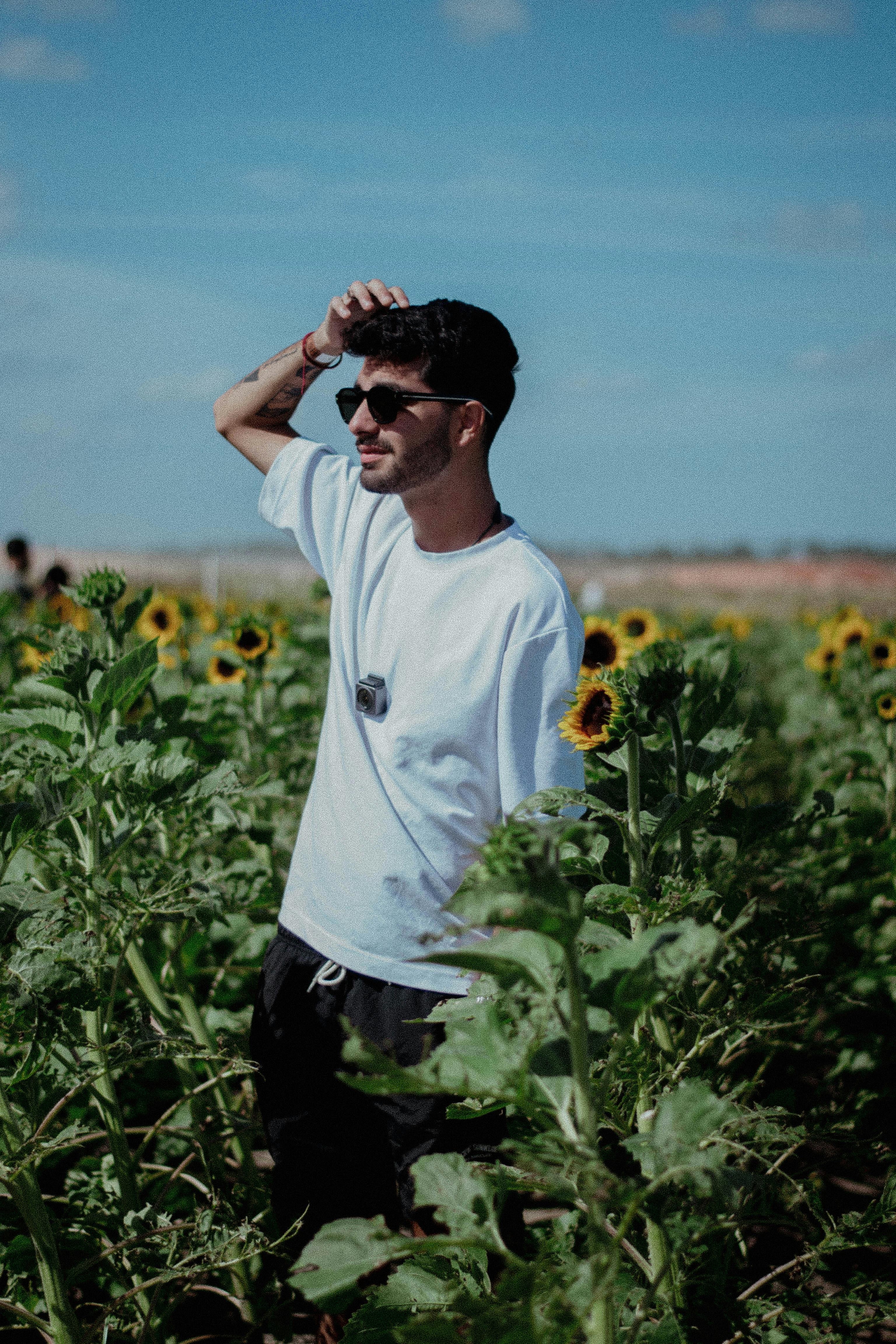 Young man with sunglasses in a sunny sunflower field, enjoying the summer day.