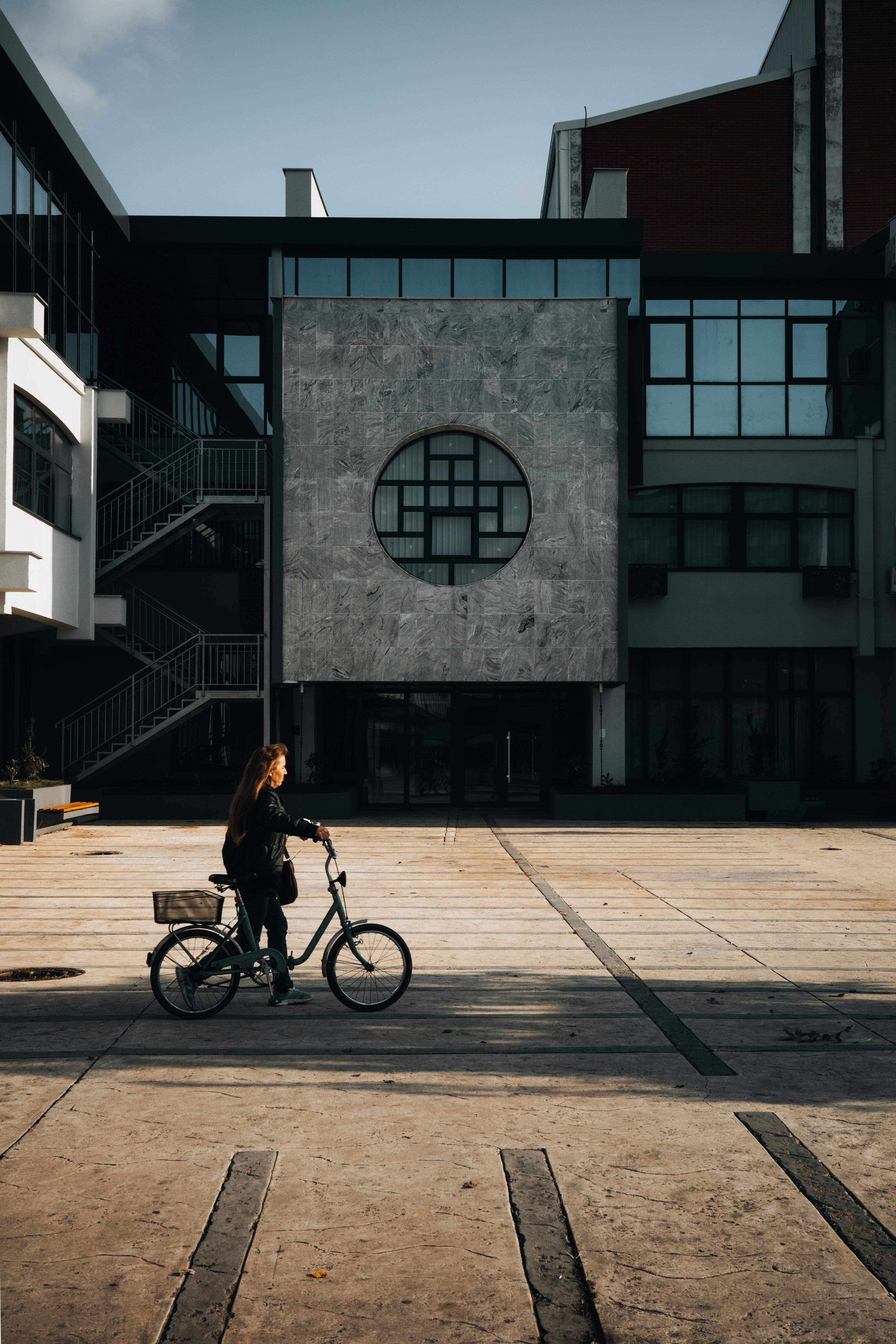 Woman riding a bicycle in a modern city courtyard with geometric architecture.