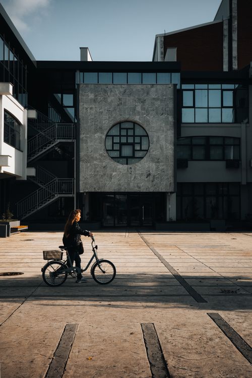 Free Woman riding a bicycle in a modern city courtyard with geometric architecture. Stock Photo