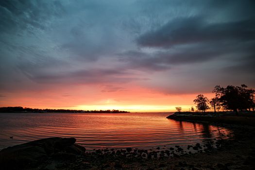 Beautiful sunrise at Stamford's shoreline with vibrant sky and calm water reflections.