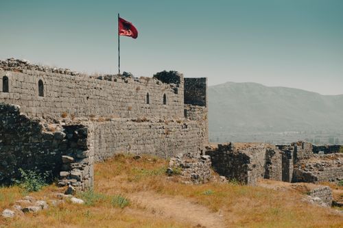 Free Historic Shkodra Castle ruins with Albanian flag, overlooking mountains. Stock Photo