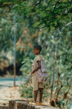 A young child in a school uniform standing outdoors in Bujumbura, Burundi, holding a book bag.