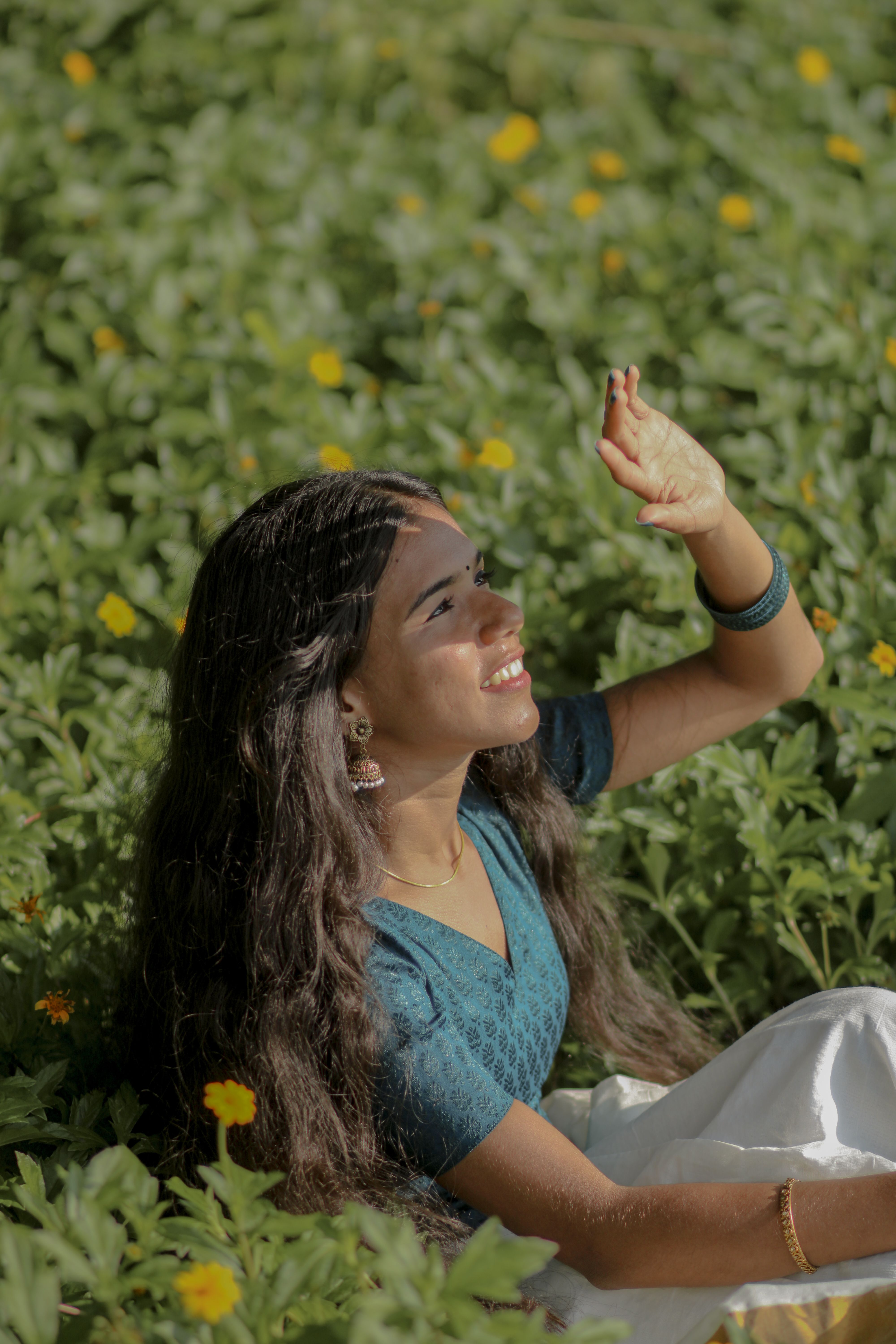 A smiling young woman enjoying sunny day in a flowery field in Kerala, India.