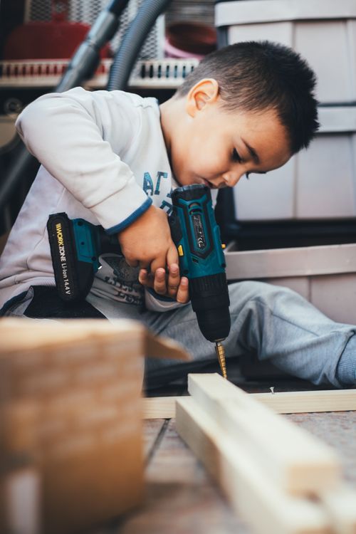 Free A young boy learning carpentry indoors, using a drill on wood. Stock Photo