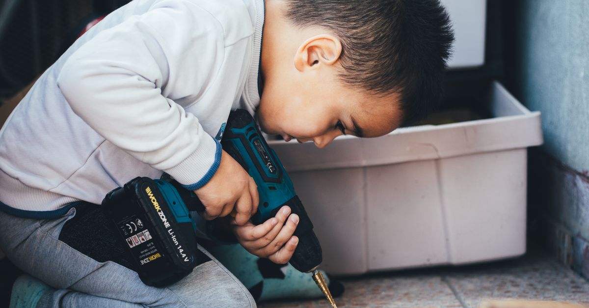 Un jeune garçon concentré sur l'utilisation d'une perceuse électrique pour un projet de menuiserie à l'intérieur.