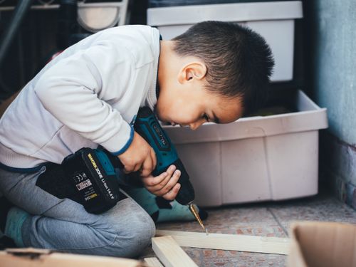 Free A young boy focused on using a power drill for a woodworking project indoors. Stock Photo