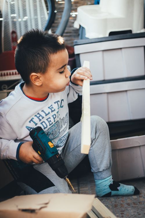 Free A young boy intently working on a DIY woodworking project with a drill indoors. Stock Photo