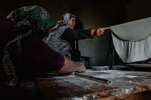 Free Women in traditional attire making bread in a rustic kitchen setting. Stock Photo