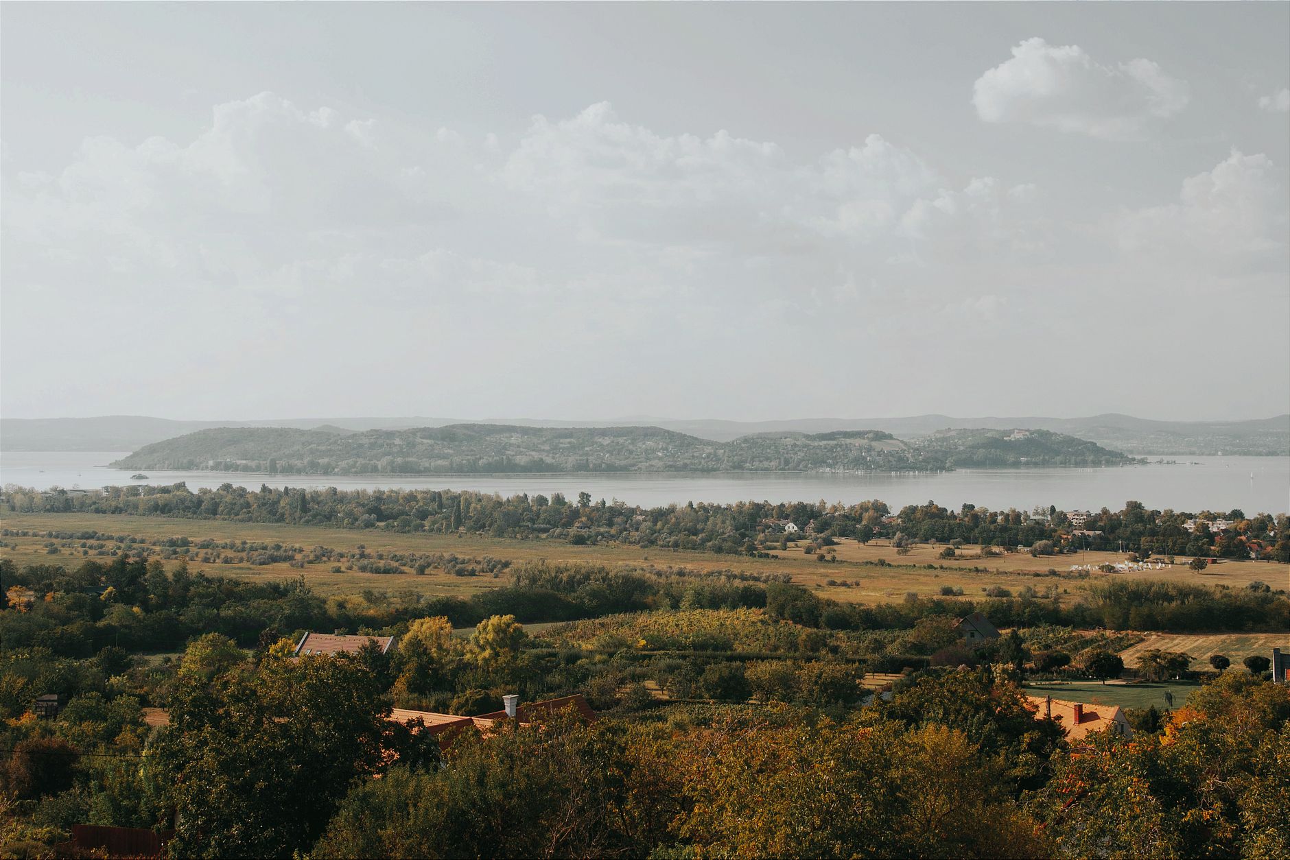 Beautiful landscape view of Lake Balaton with lush greenery and hills under a cloudy sky.