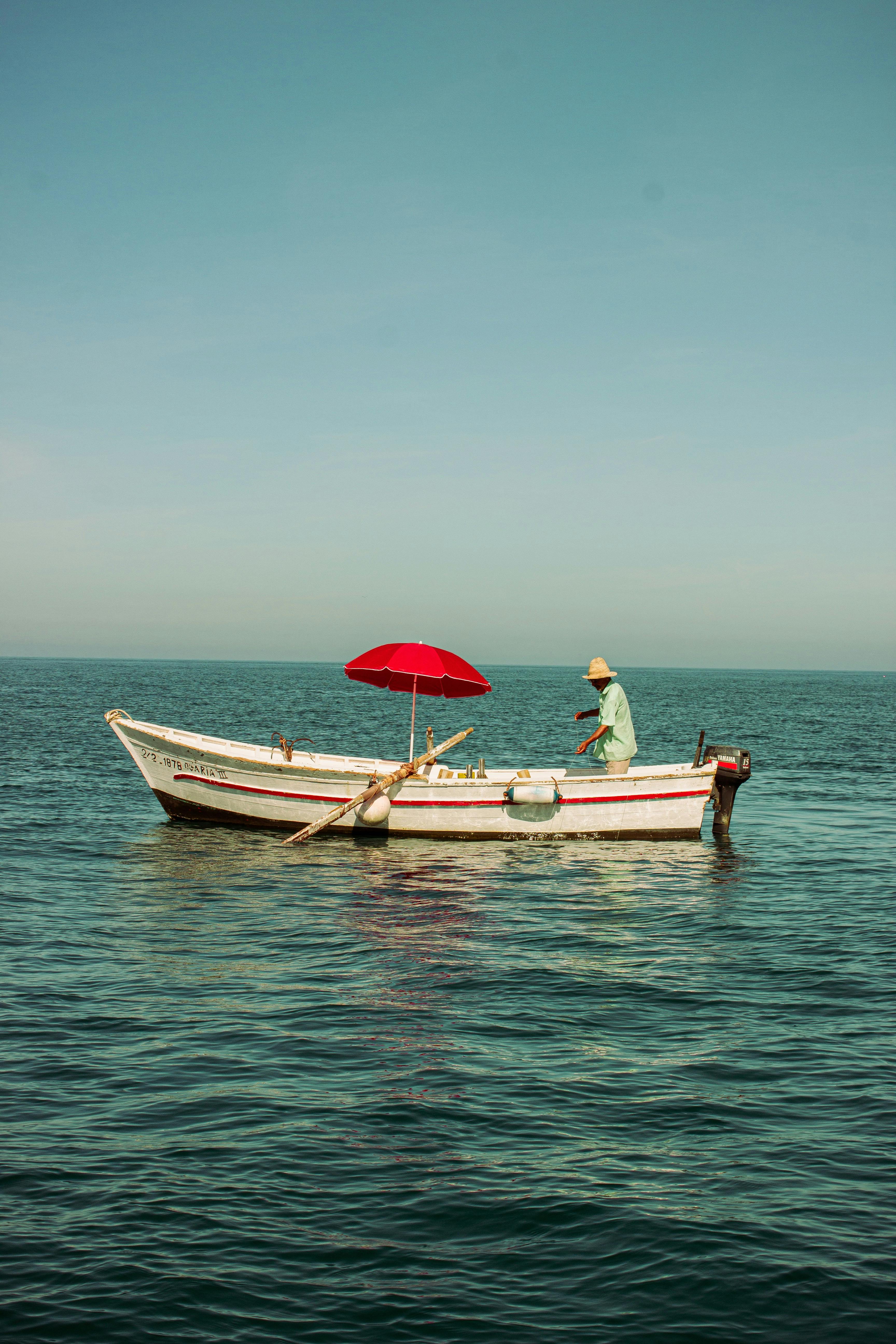 A serene scene of a solo fisherman on a small boat with a red umbrella on the Moroccan sea.