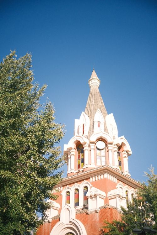 Free A vintage red brick architectural tower against a bright blue sky and green trees. Stock Photo