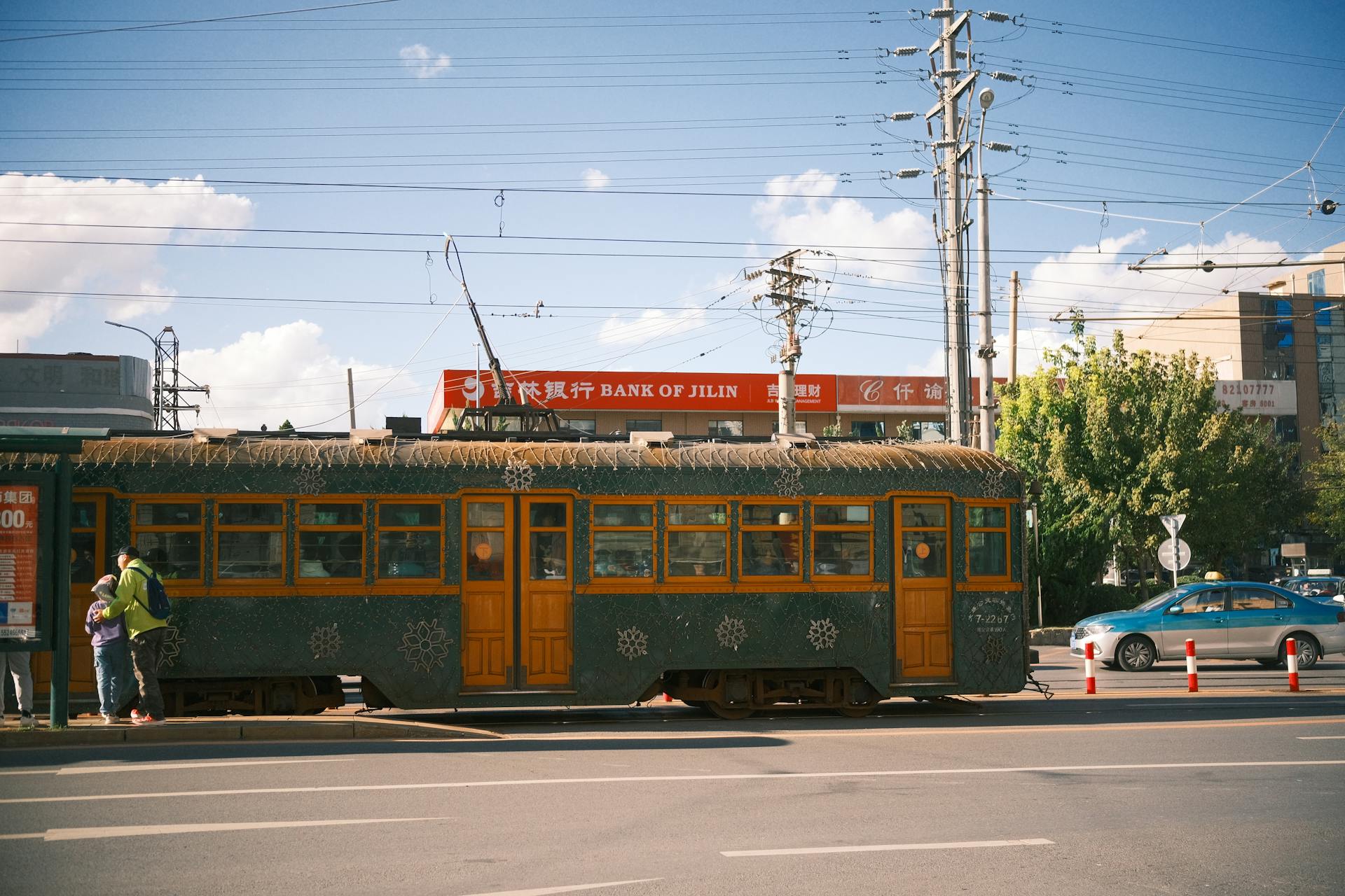 Vintage tram travels through city street near Bank of Jilin under clear skies.