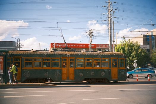 A classic vintage tram on a sunny day urban street with people nearby.