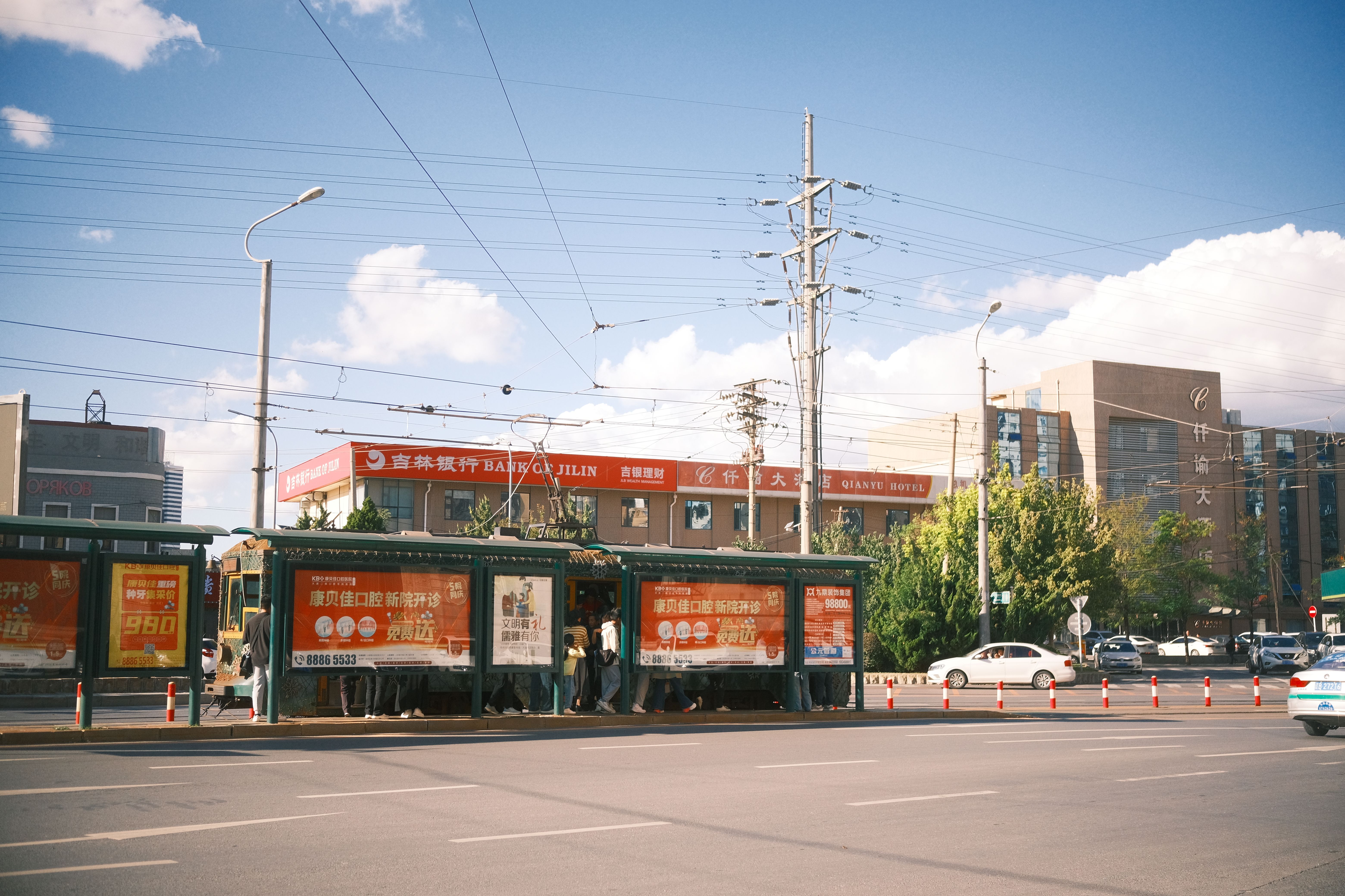 Street view of a busy bus stop with a cityscape backdrop on a sunny day.