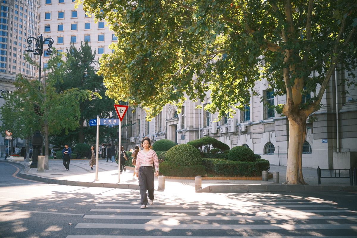 A pedestrian crossing a sunlit street in a bustling downtown. Photo by mitbg000 on Pexels