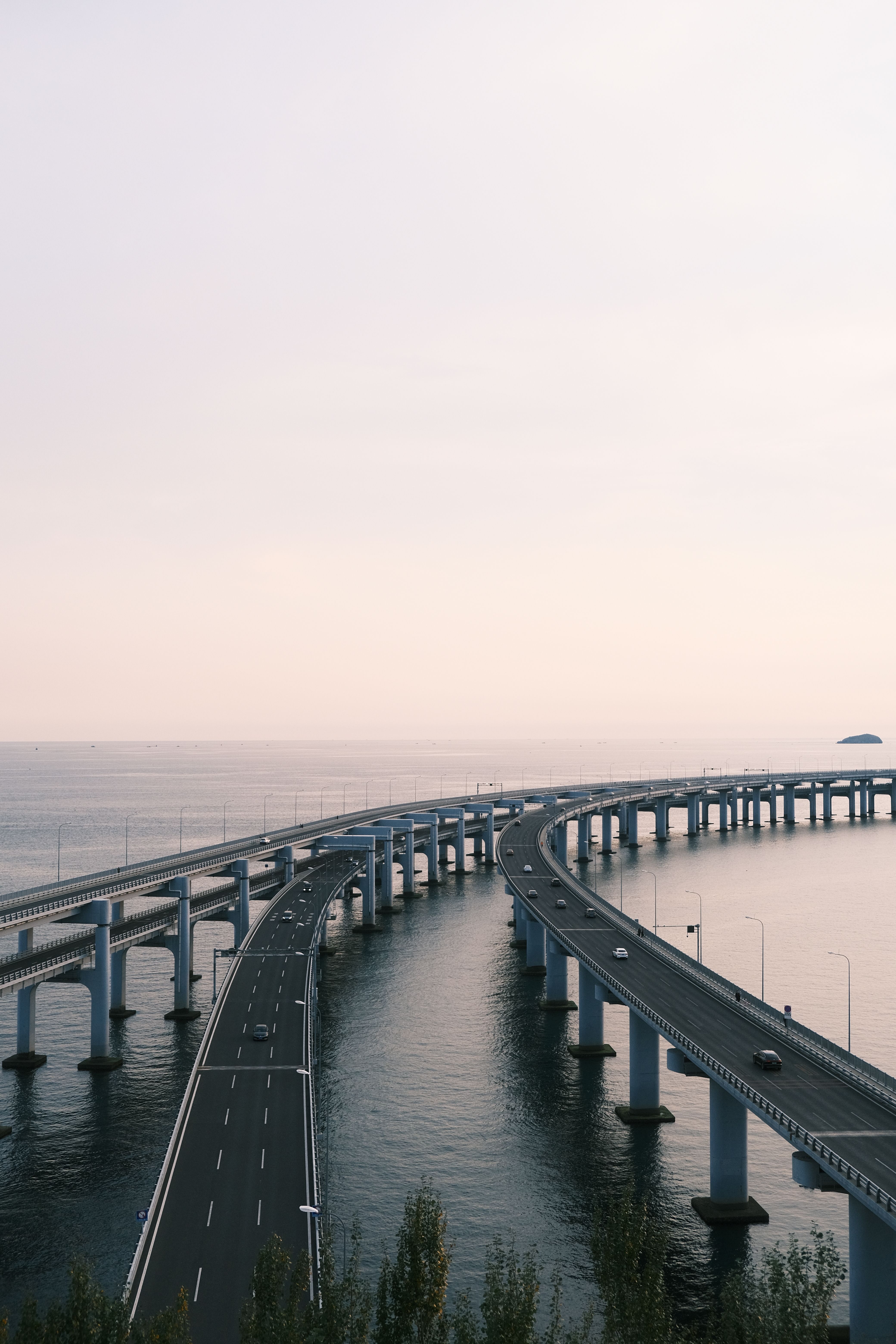 Aerial view of a highway curving over the ocean against a pastel sky, conveying tranquility.