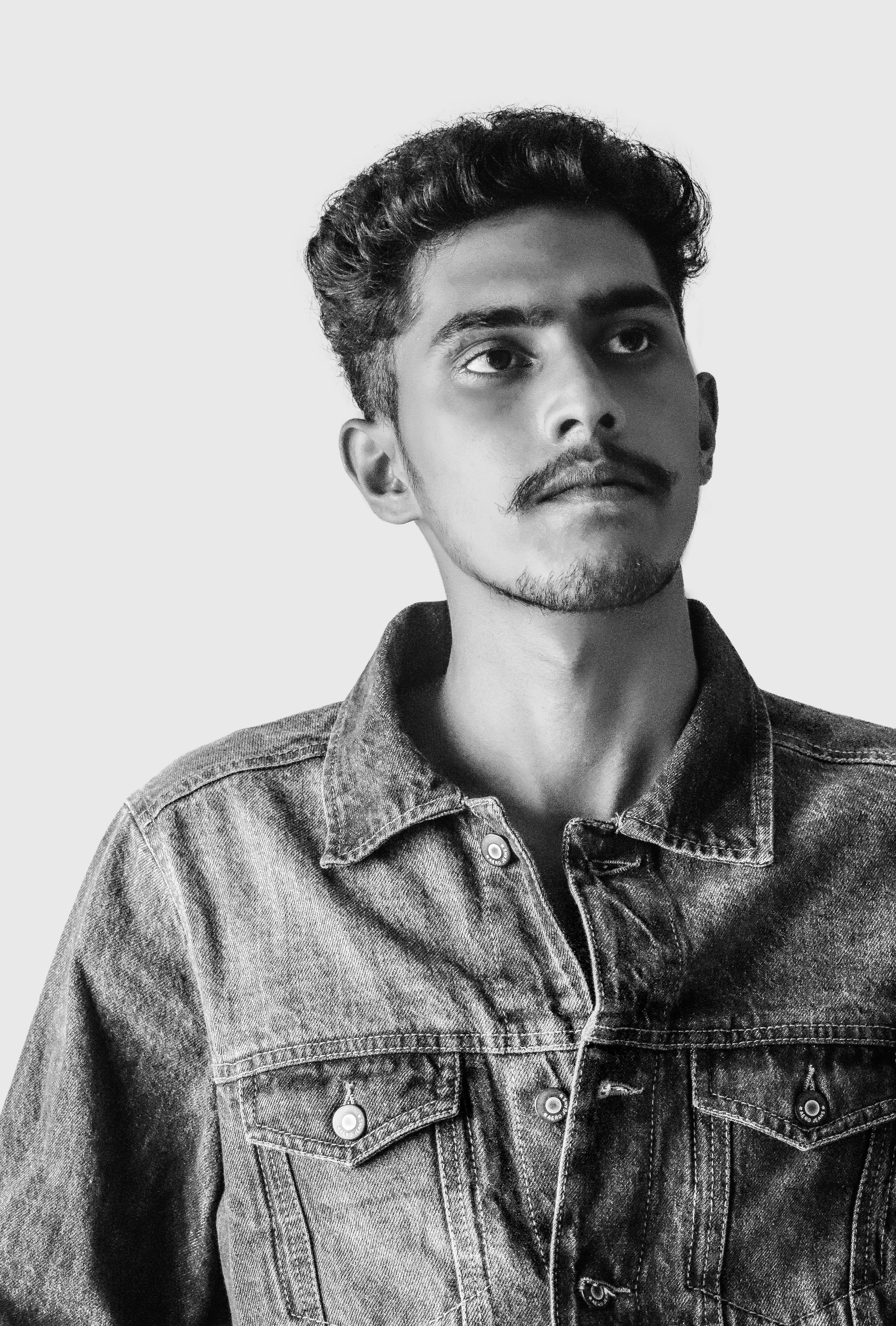 Artistic black and white portrait of a young man wearing a denim jacket, looking upwards.