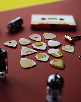Collection of guitar picks with a vintage cassette and audio tubes on red backdrop.