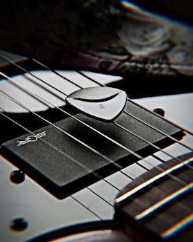 Detailed image of an electric guitar close-up featuring a guitar pick on the strings.