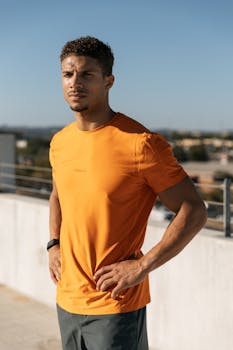 Fit man in orange shirt poses confidently on rooftop in Austin, Texas during a sunny day.