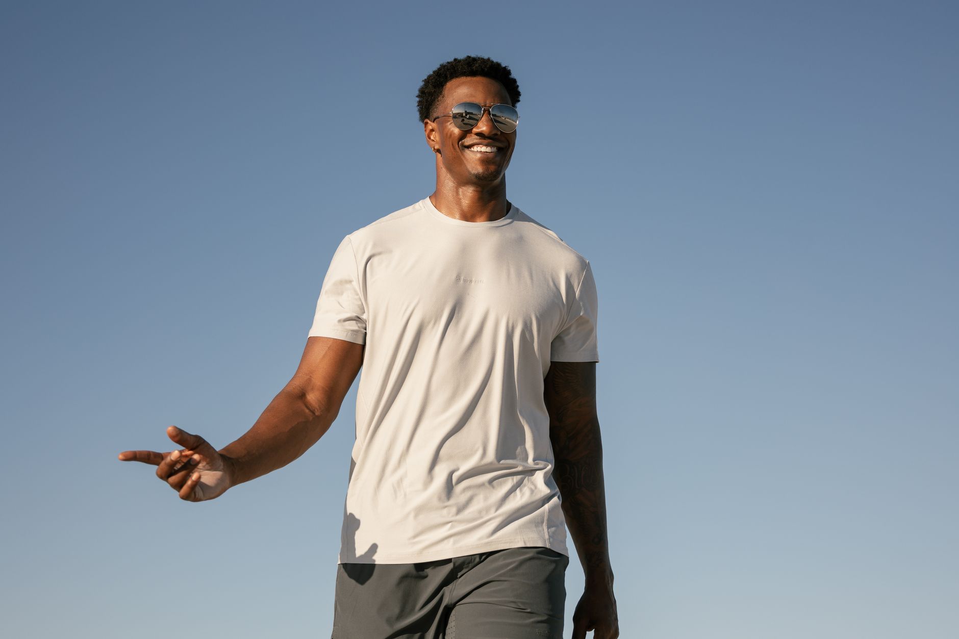 A cheerful man in casual wear enjoys a sunny day outdoors with clear blue skies.