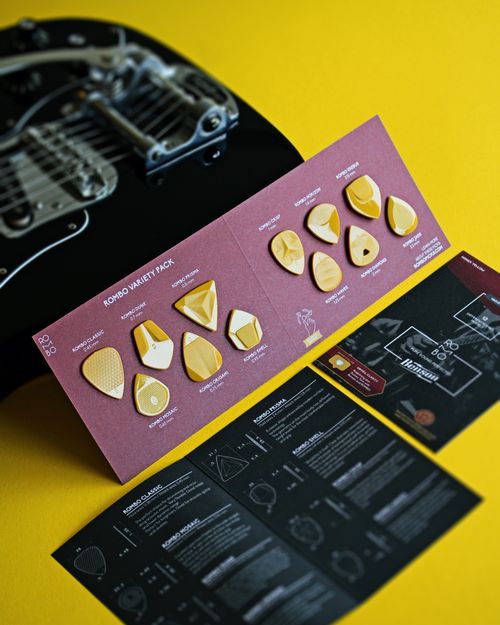 Free A selection of unique guitar picks displayed on a yellow surface next to an electric guitar. Stock Photo