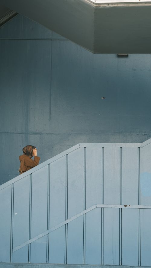 Free A person walks up a blue stairwell in a minimalist architectural setting. Stock Photo