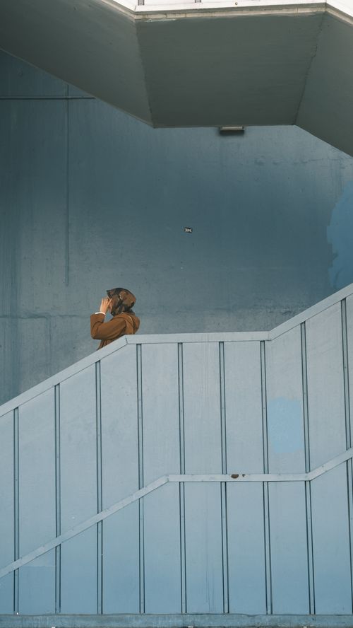 Free A person in a brown hoodie stands on a modern staircase, talking on the phone. Stock Photo