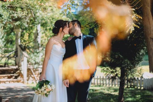 Free Newlywed couple shares a romantic kiss in a sunlit garden, symbolizing love and unity. Stock Photo