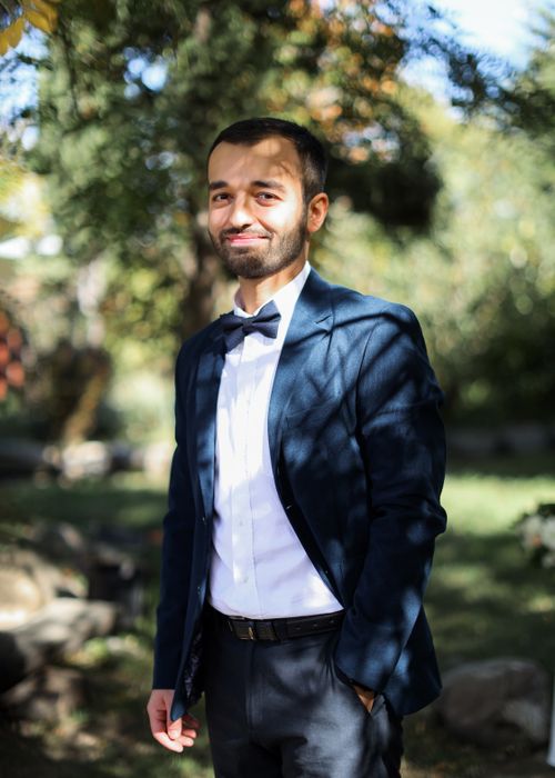 Free Young man in a dark suit and bow tie standing outside under sunlight with a subtle smile. Stock Photo