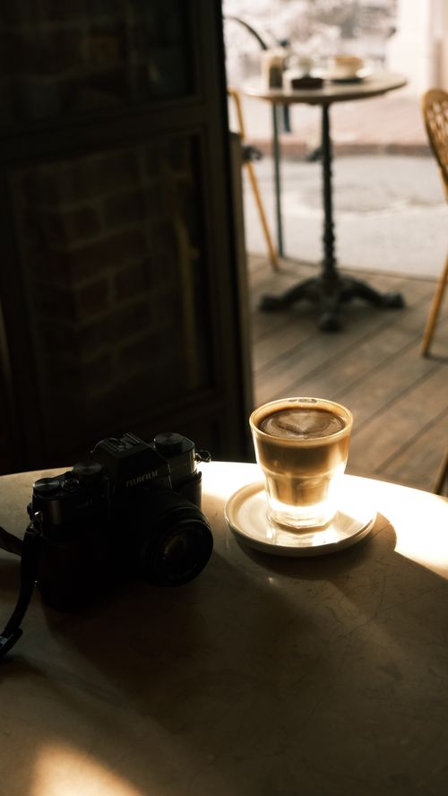 Free A coffee and vintage camera on a sunlit table in a cozy cafe, inviting ambiance. Stock Photo