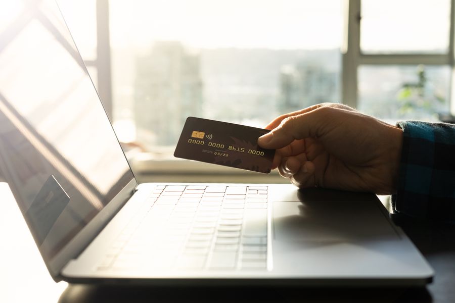 A hand holding a credit card in front of a laptop, symbolizing online shopping and digital payment.