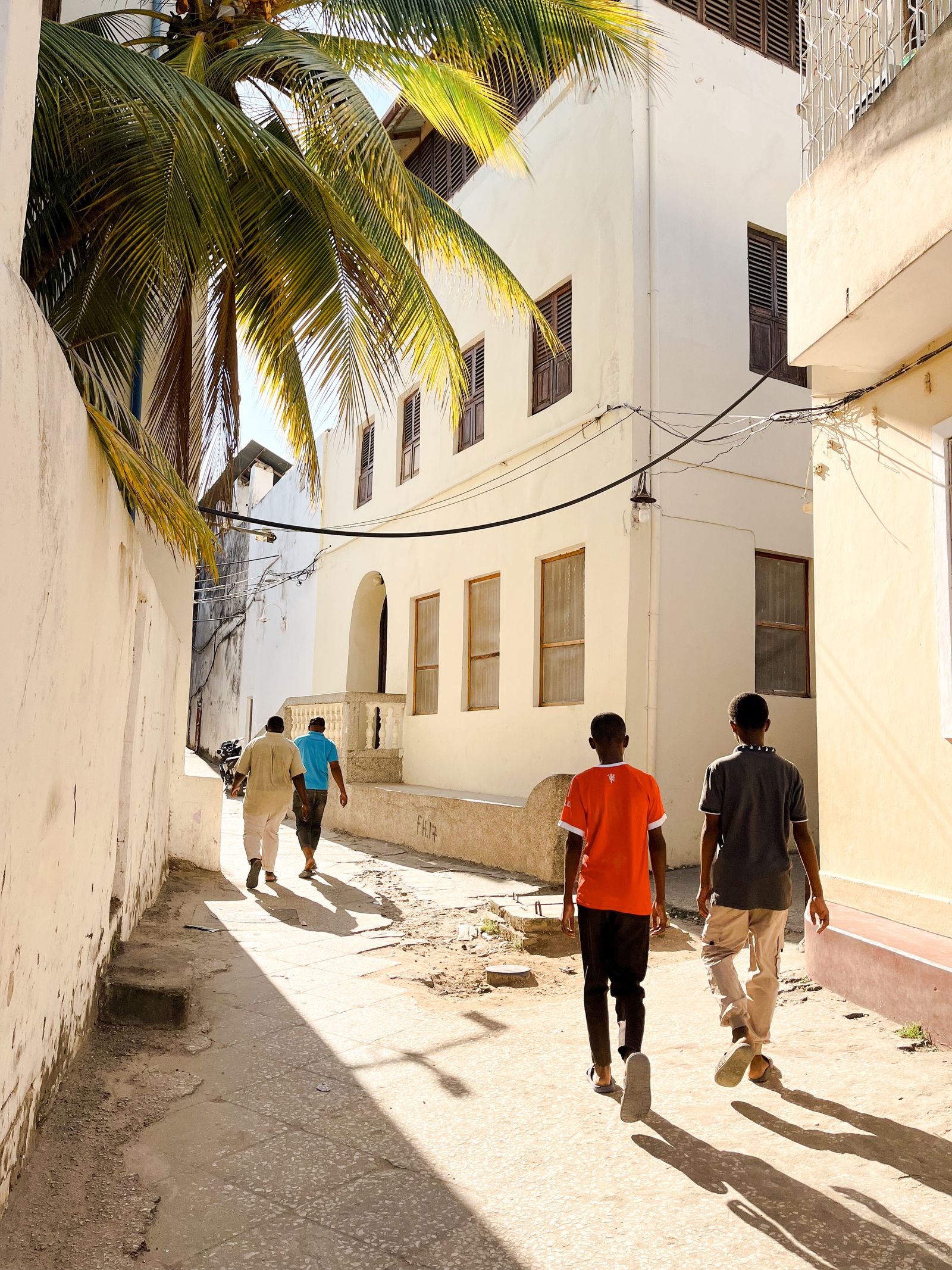 Sunny street scene in Stone Town, Zanzibar, with people walking beneath old buildings