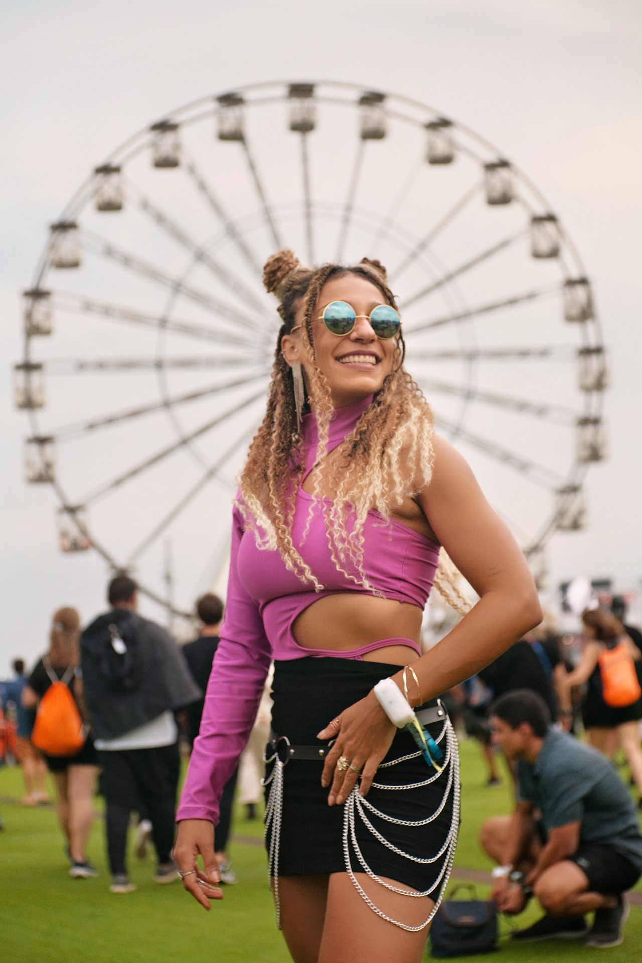 Smiling woman in a bright pink top and black mini skirt with a chain belt at a summer outdoor concert with a Ferris wheel