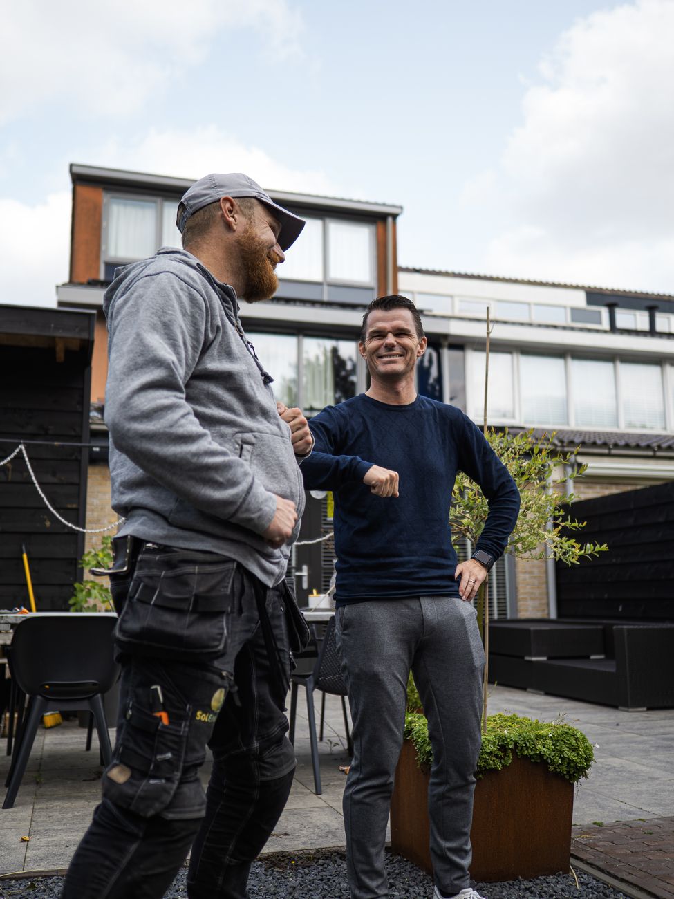 Twee mannen delen een ellebooggroet buiten en tonen kameraadschap en vriendelijkheid.