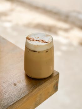 A refreshing iced coffee topped with foam and cinnamon powder on a wooden table.
