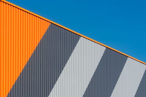 Free Abstract view of a modern industrial facade with orange and gray stripes under a clear blue sky. Stock Photo