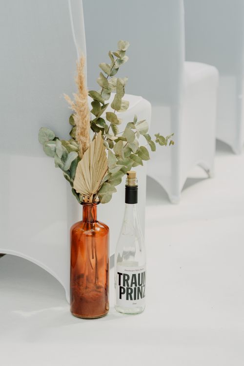 Free Elegant dried floral arrangement in amber glass bottle beside printed bottle. Stock Photo
