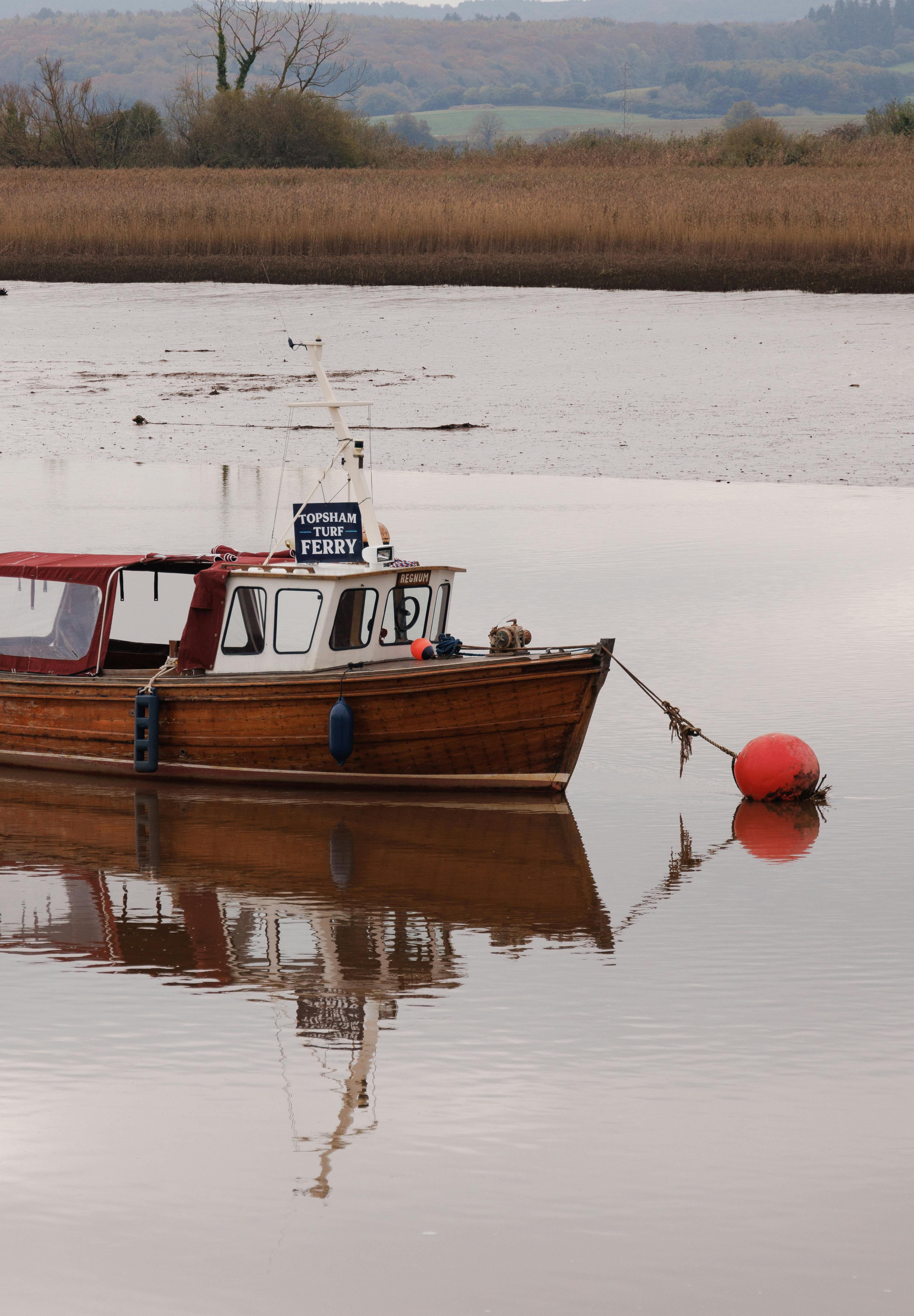 Free Wooden ferry boat anchored on a tranquil river with scenic reflection. Stock Photo
