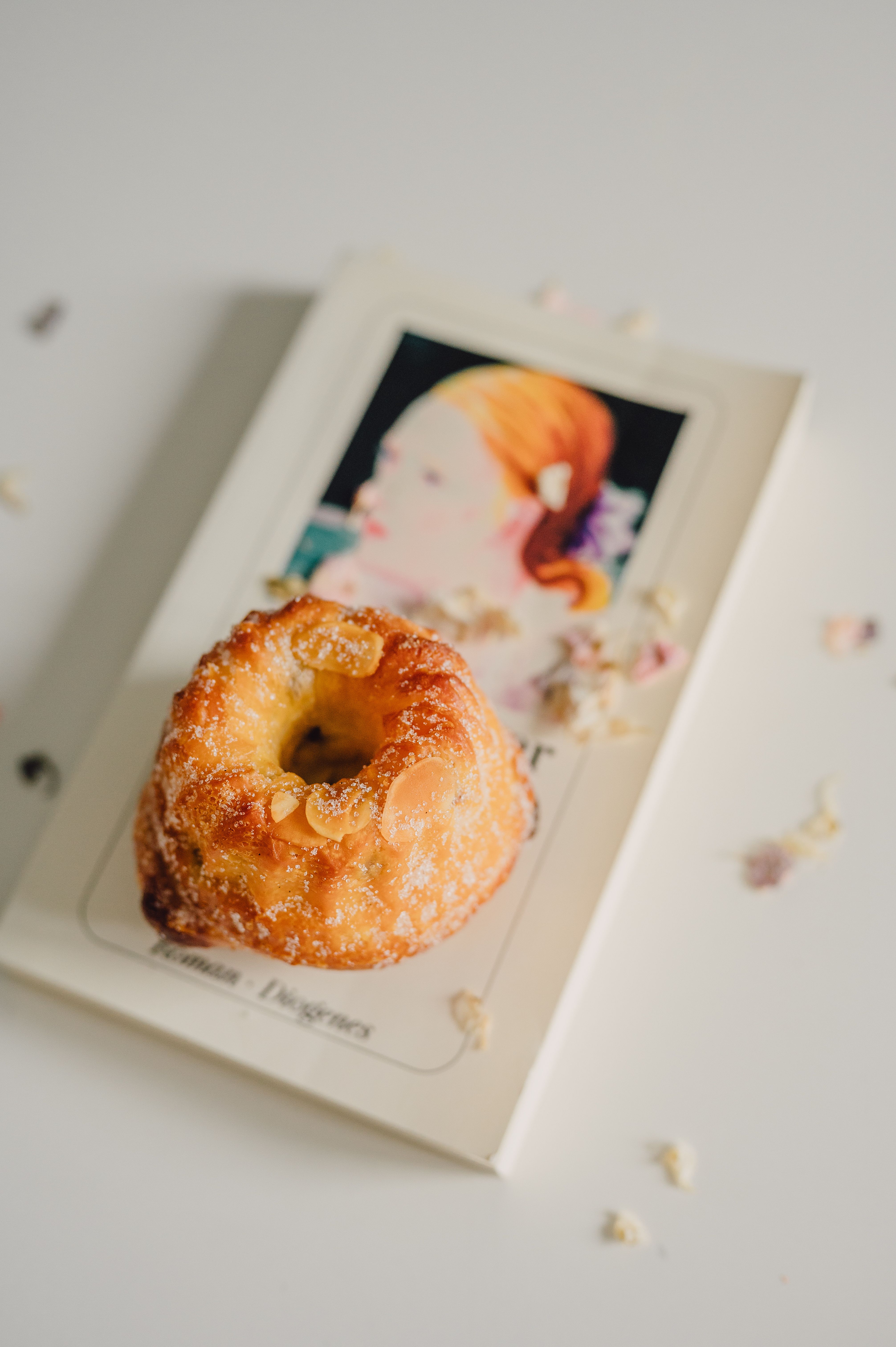 Golden pastry atop a book featuring art, surrounded by delicate floral touches on white surface.